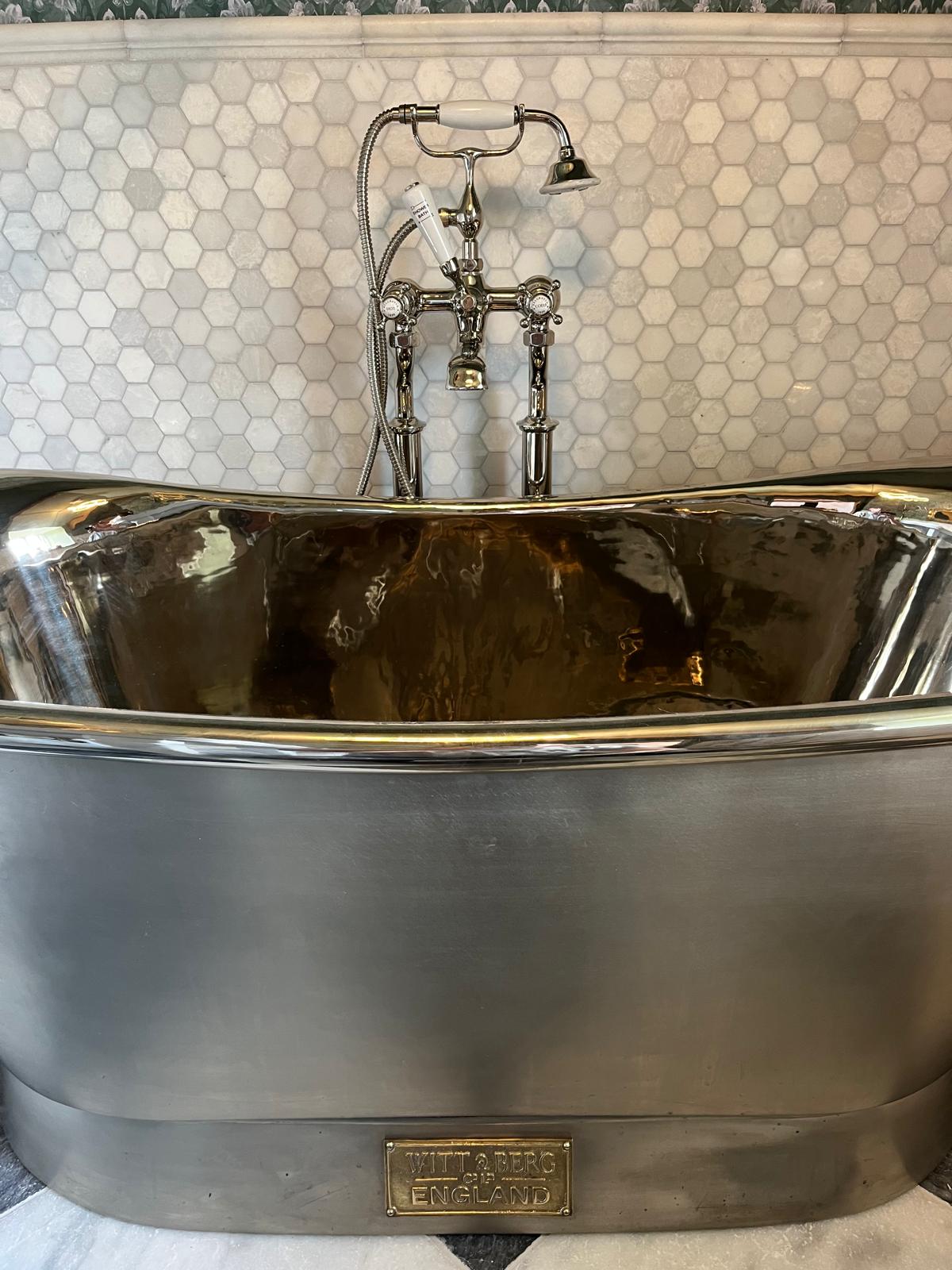Polished tin bath with traditional nickel mixer against marble mosaic