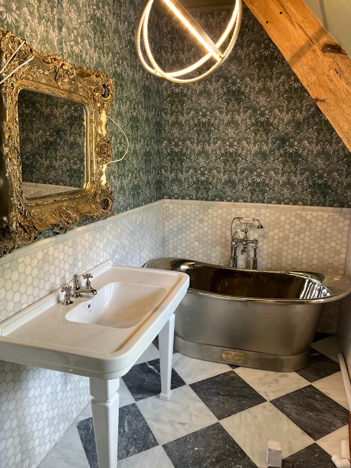 Polished tin bateau bath with console basin, gilt mirror and chequerboard marble floor