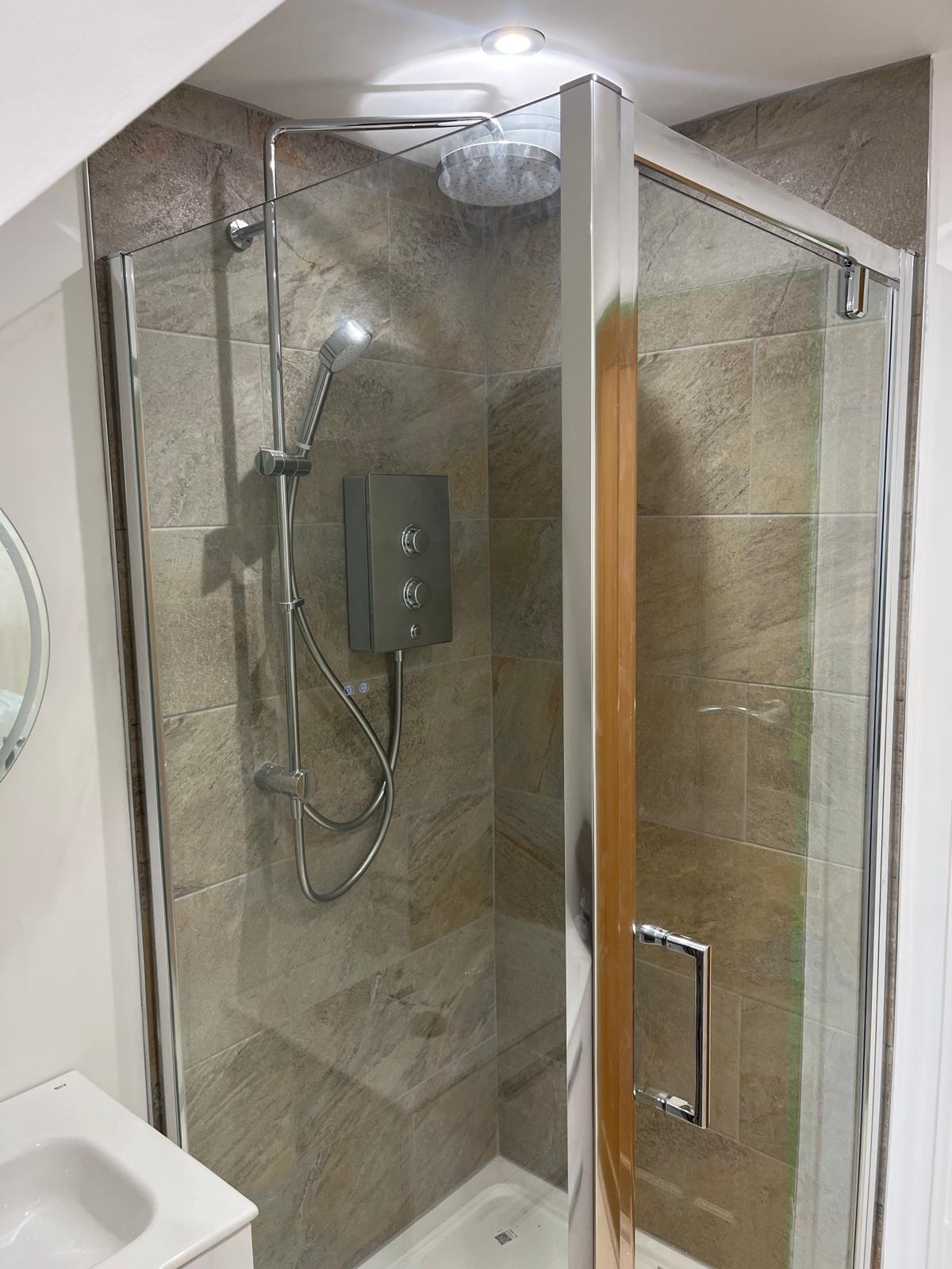 Corner shower with stone-effect tiles and rainfall head in a loft en-suite